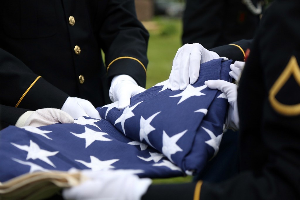 Military personnel in dress uniforms and white gloves carefully folding the American flag during a ceremony.